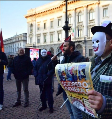 Un uomo con una maschera da clown tiene uno striscione "sciopero generale".